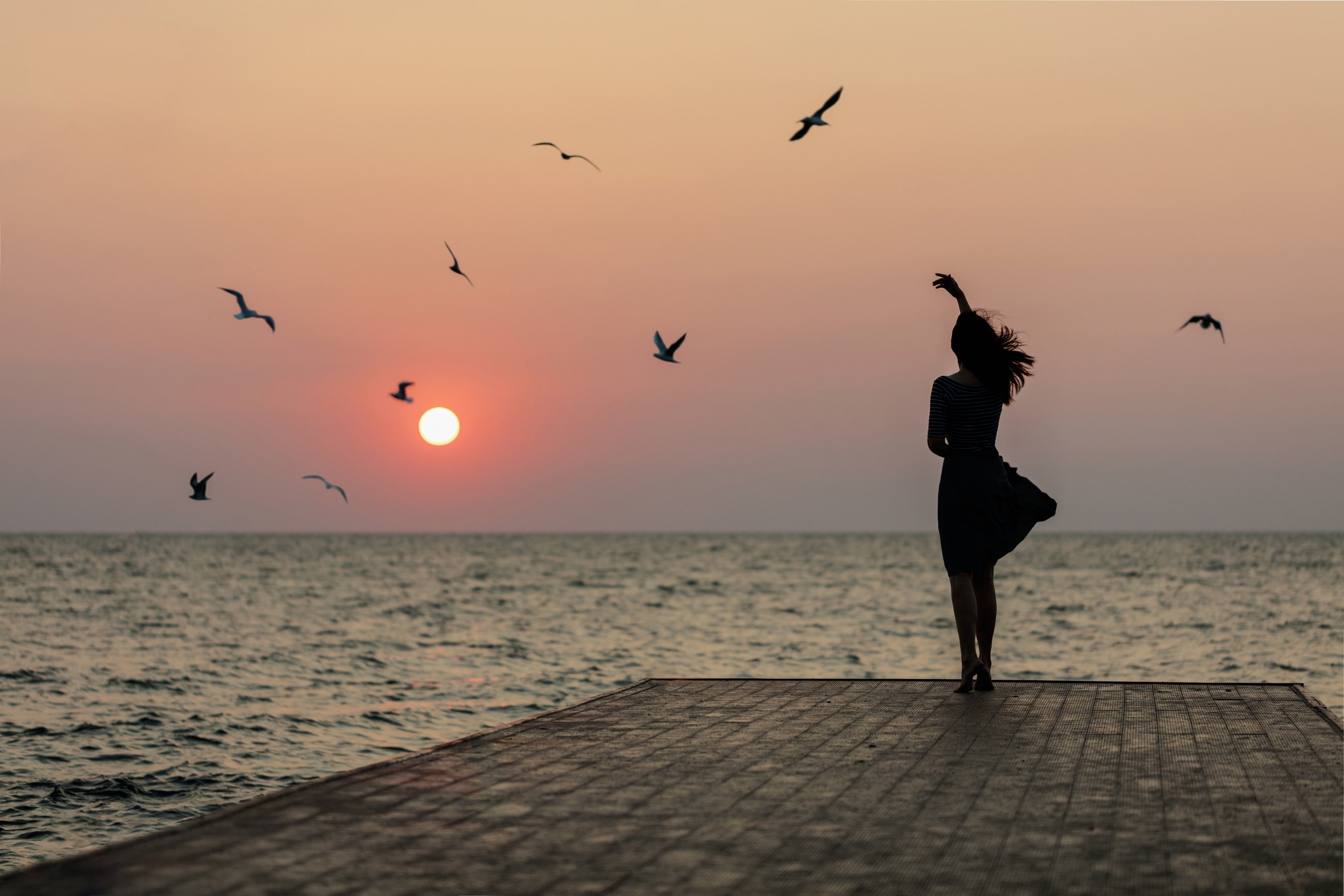 Silhouette of a girl on a sunset background (sunrise) on the sea, horizon line.